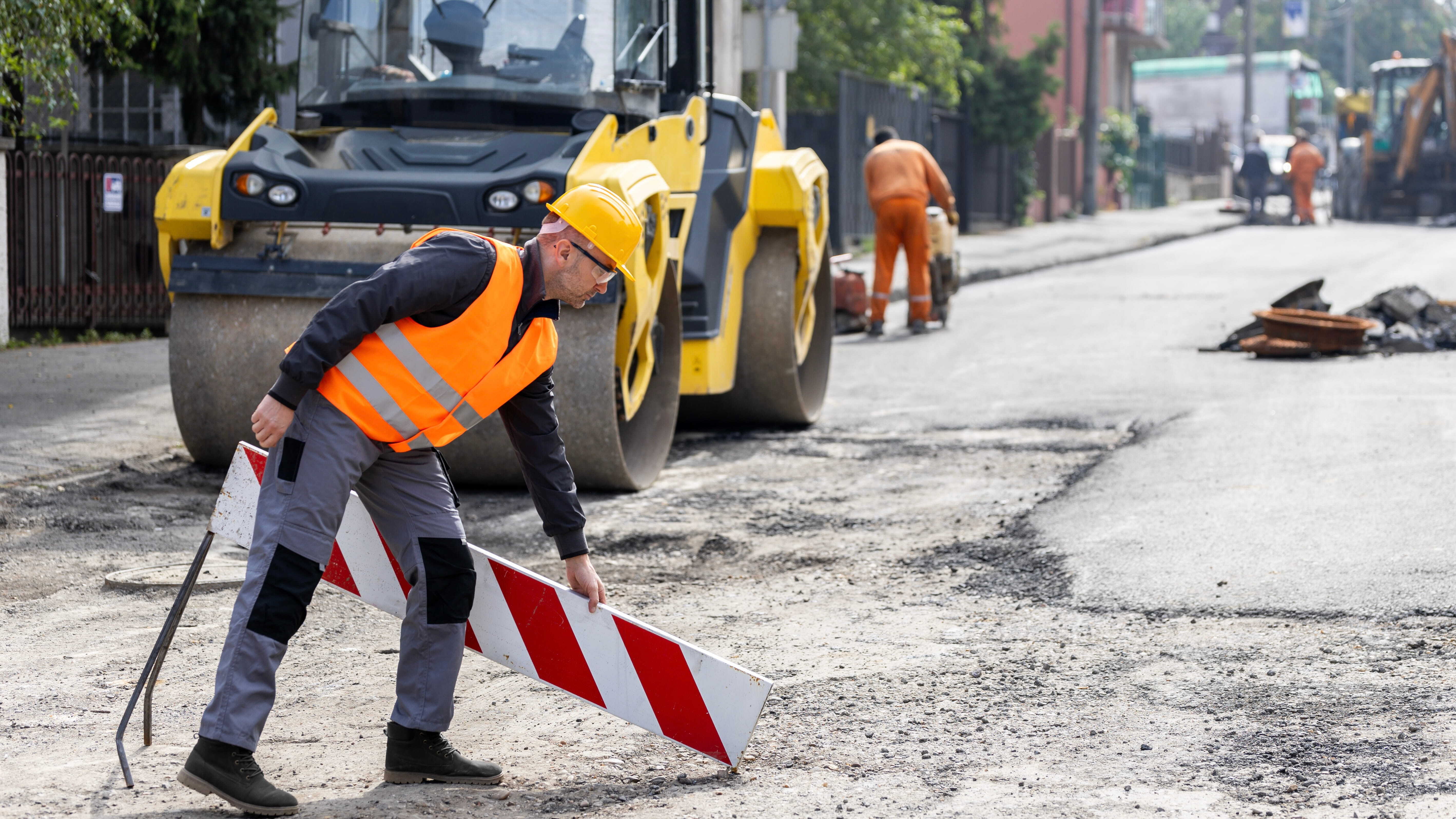 construction worker setting up a traffic barrier during street repair in an urban area on a clear day