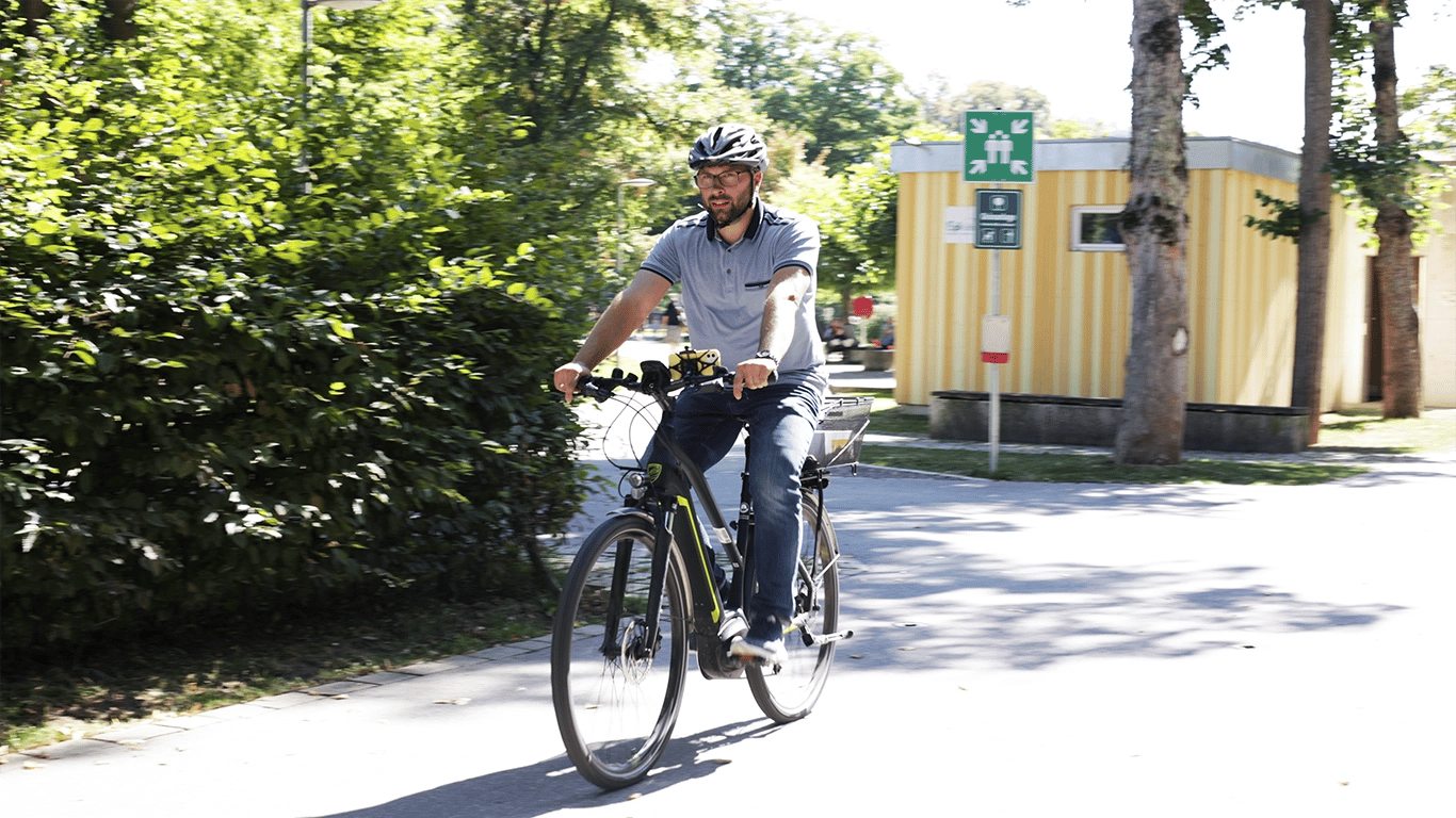 A cyclist riding on a paved path with a smartphone mounted to the handlebars running the vialytics app for automated road damage detection.