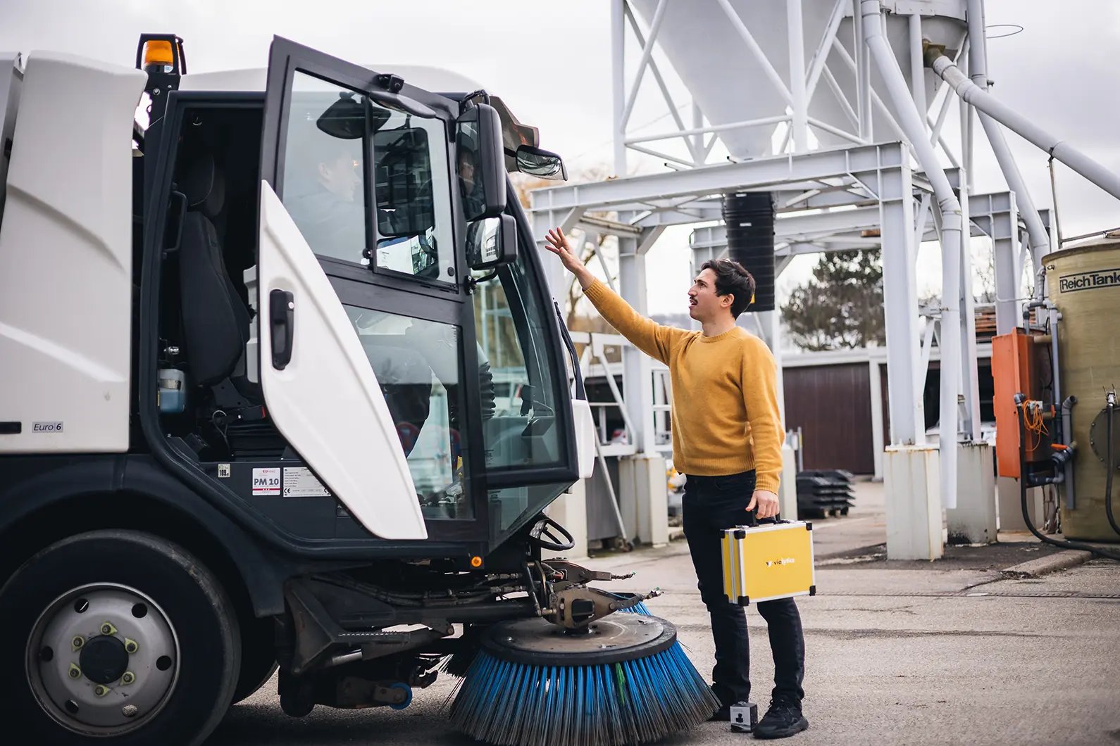 a man stands in front of a road sweeper on a building yard and hold the vialytics case in his hands
