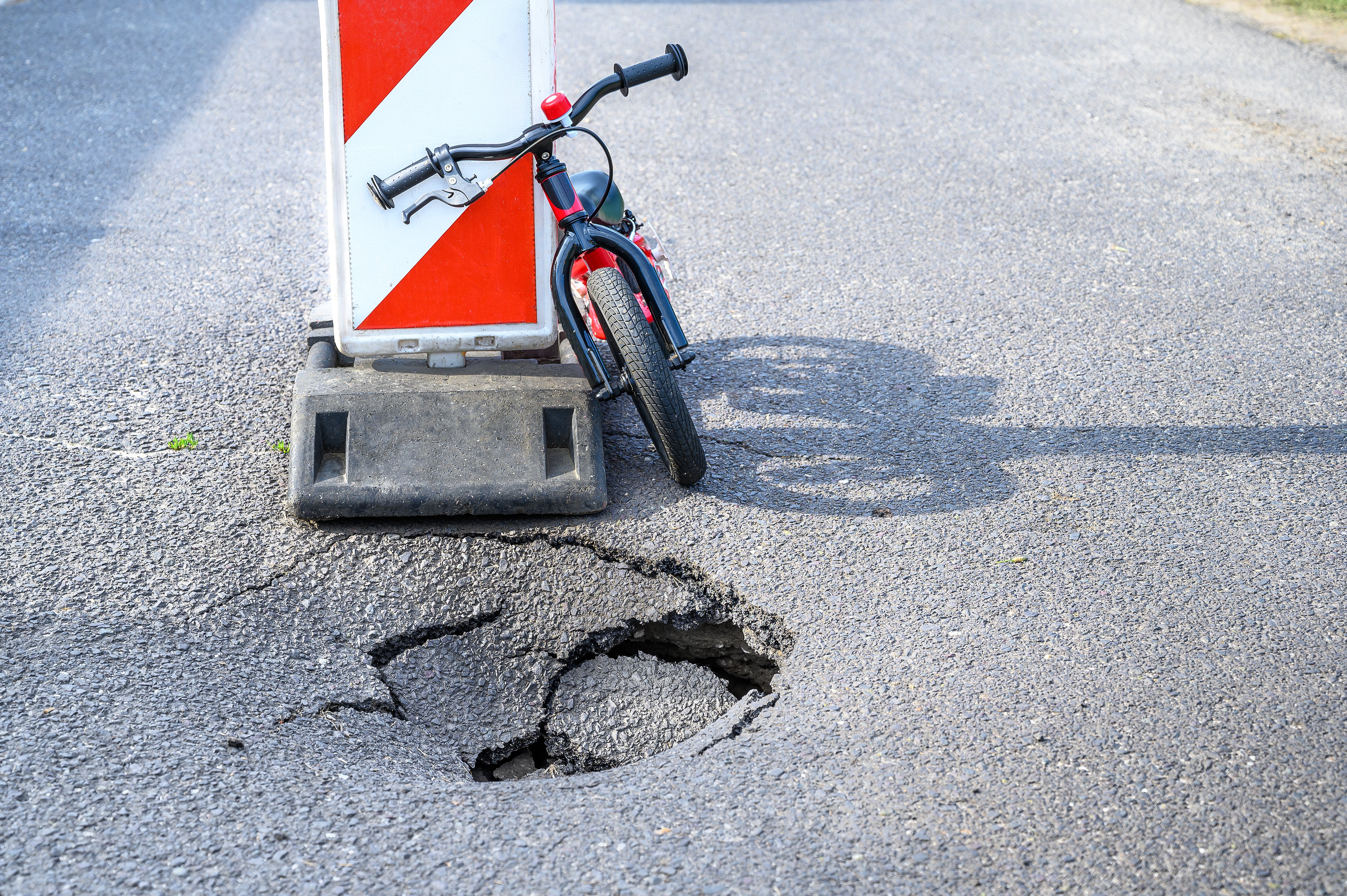 a childs bike next to a pot hole and a warning road sign