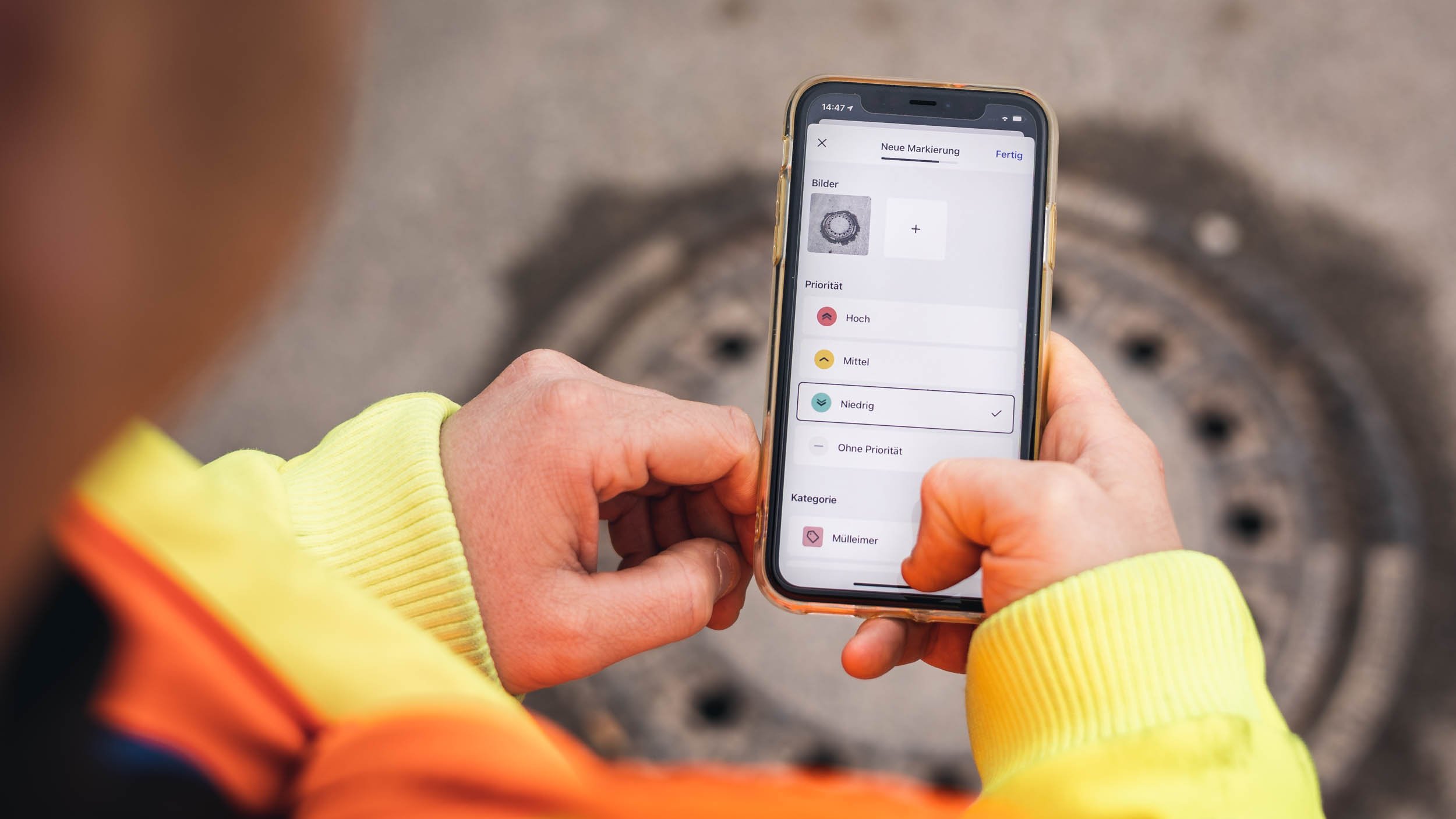 An employee from the public works department is holding a cell phone and the vialytics app is open. A manhole cover can be seen in the background