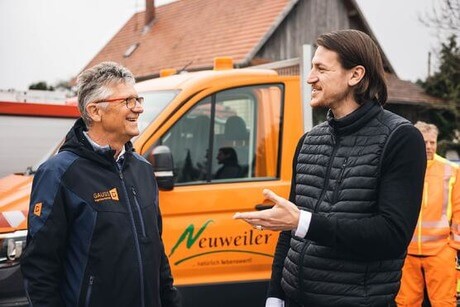 2 men talking in front of an orange vehicle