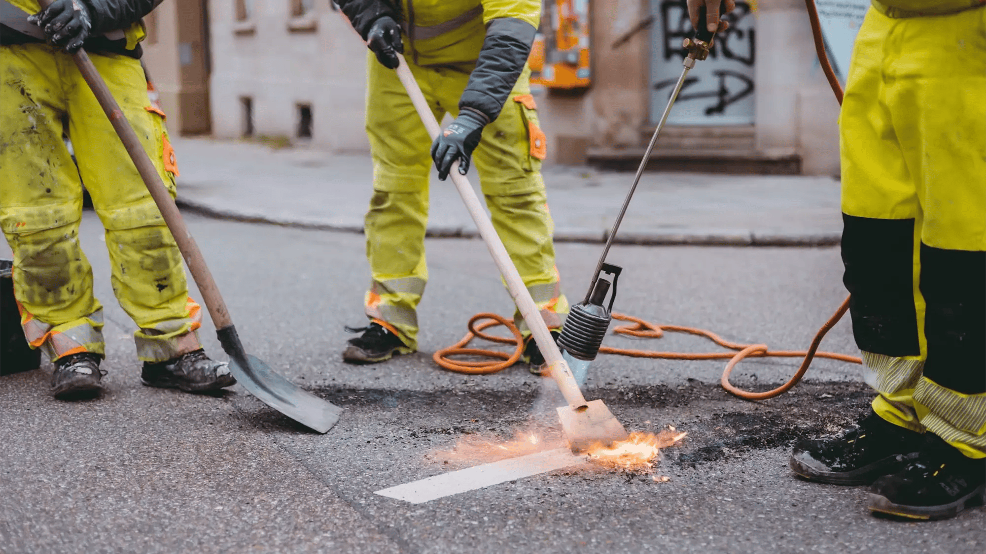 Maintenance team performing road repairs and refreshing pavement markings as part of urban infrastructure management.