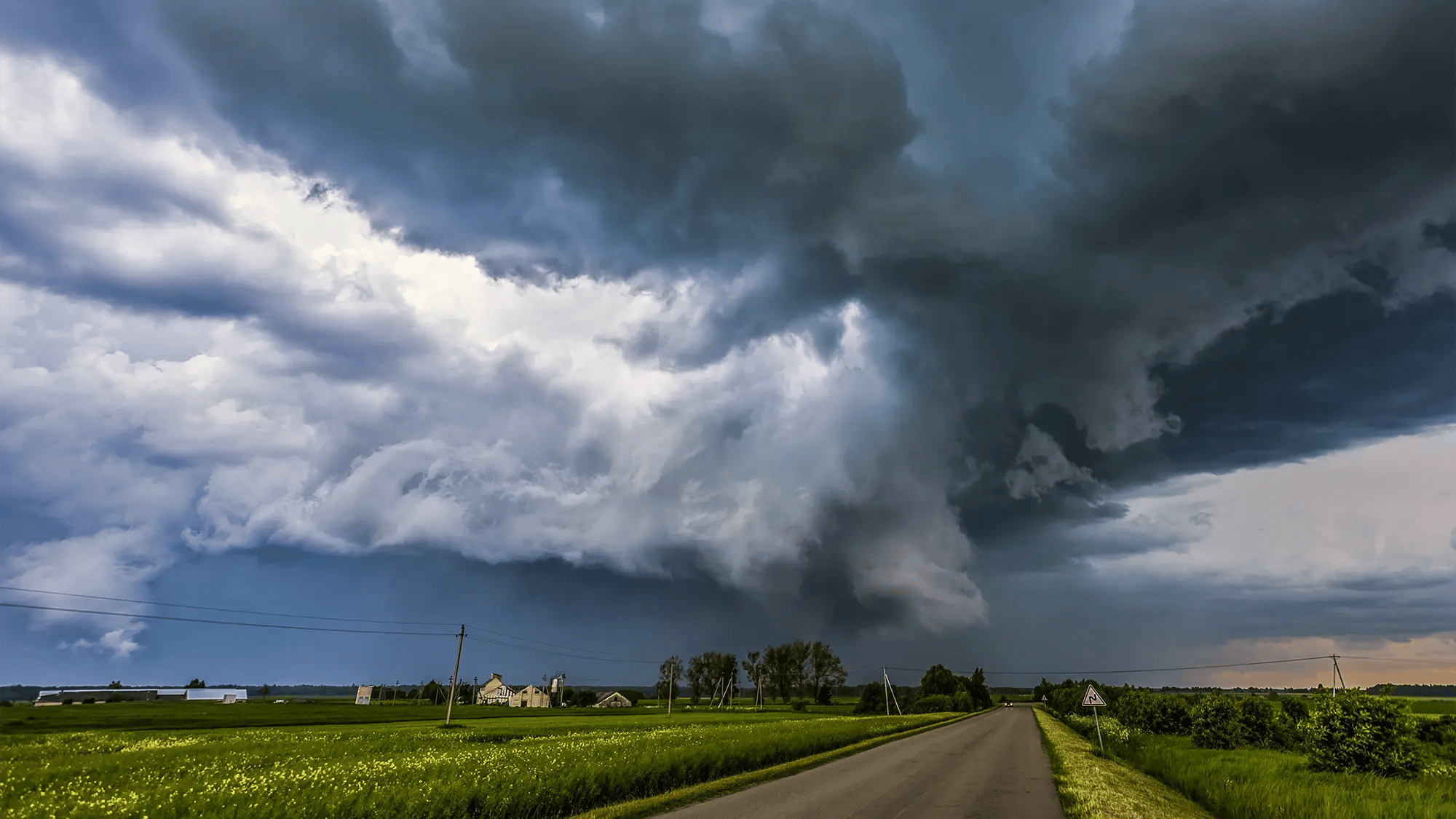 A massive, dark shelf cloud formation looming over a rural road and countryside, representing the extreme weather threats that local governments manage and prepare for using vialytics solutions.