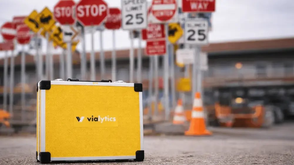 A yellow vialytics case in front of a variety of American road signs, symbolizing comprehensive traffic infrastructure management.