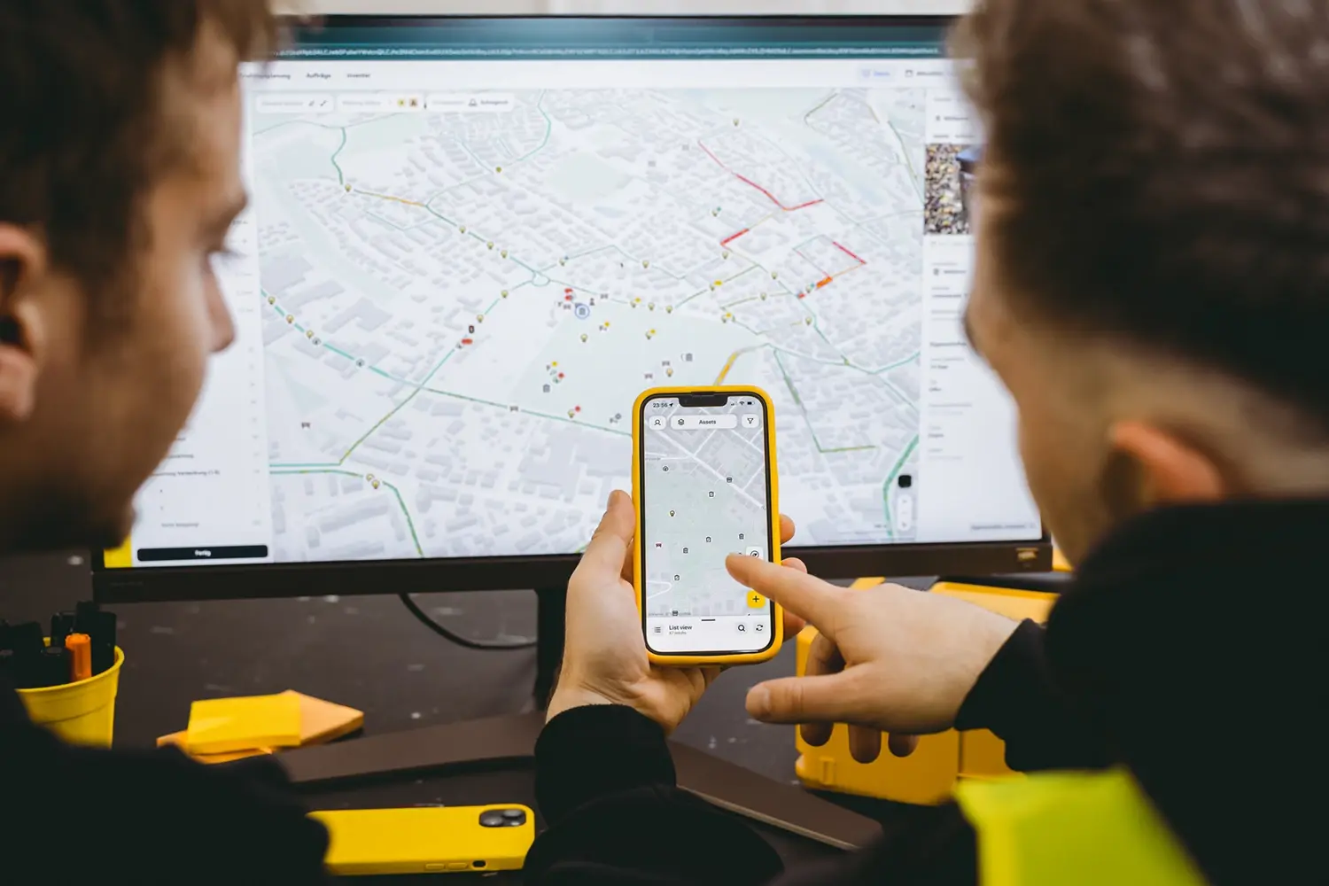 Two colleagues reviewing road network data on a smartphone and monitor in the vialytics system